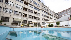 Piscina con tumbonas y sombrillas, rodeada por un edificio de varios pisos con balcones.