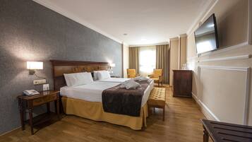 A hotel room with a large bed, bedside tables, a TV, and a wooden bench.