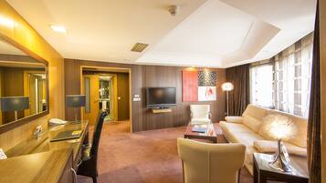 A hotel room with a wooden desk, a television, a sofa, and a lamp.