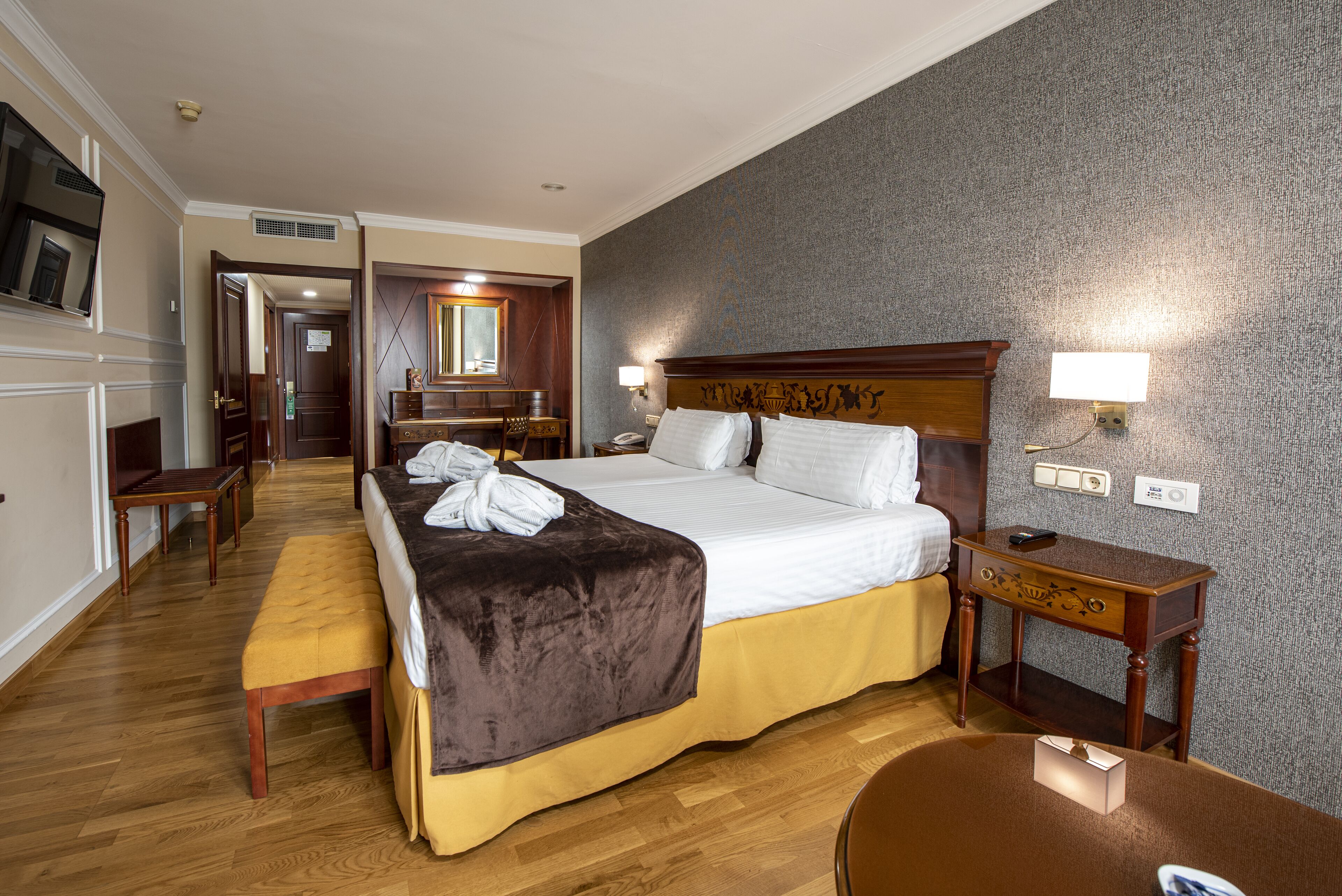 A hotel room with a large bed, a bedside table, a desk, and a chair.