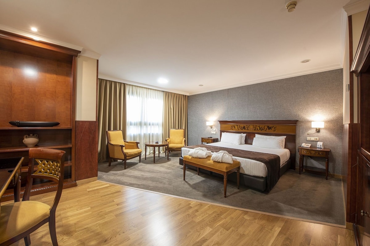 Ein Hotelzimmer mit einem großen Bett, zwei Sesseln, einem kleinen Tisch, einem Schreibtisch und einem Stuhl.