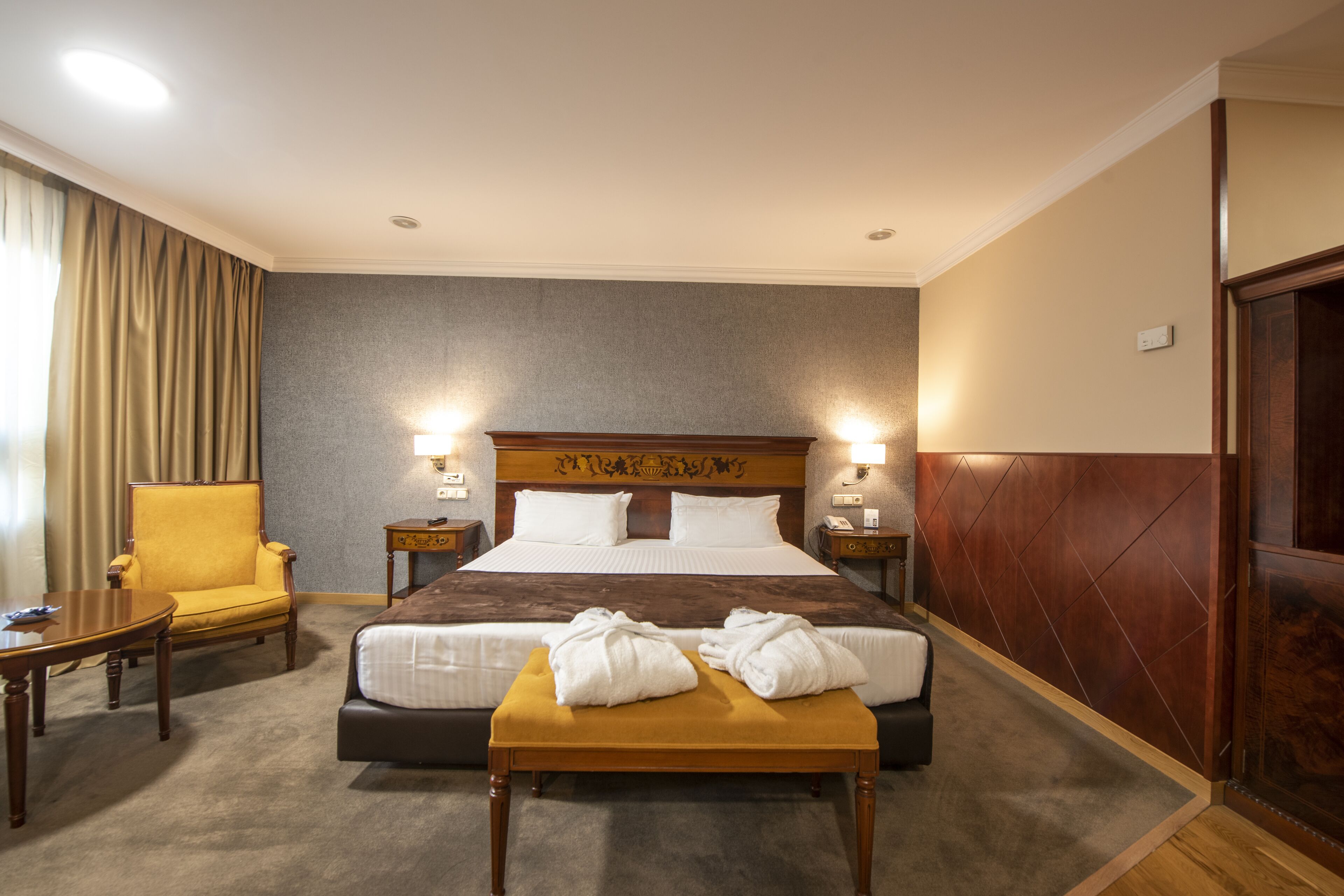 A hotel room with a large bed, a bedside table, a chair, and a small table.