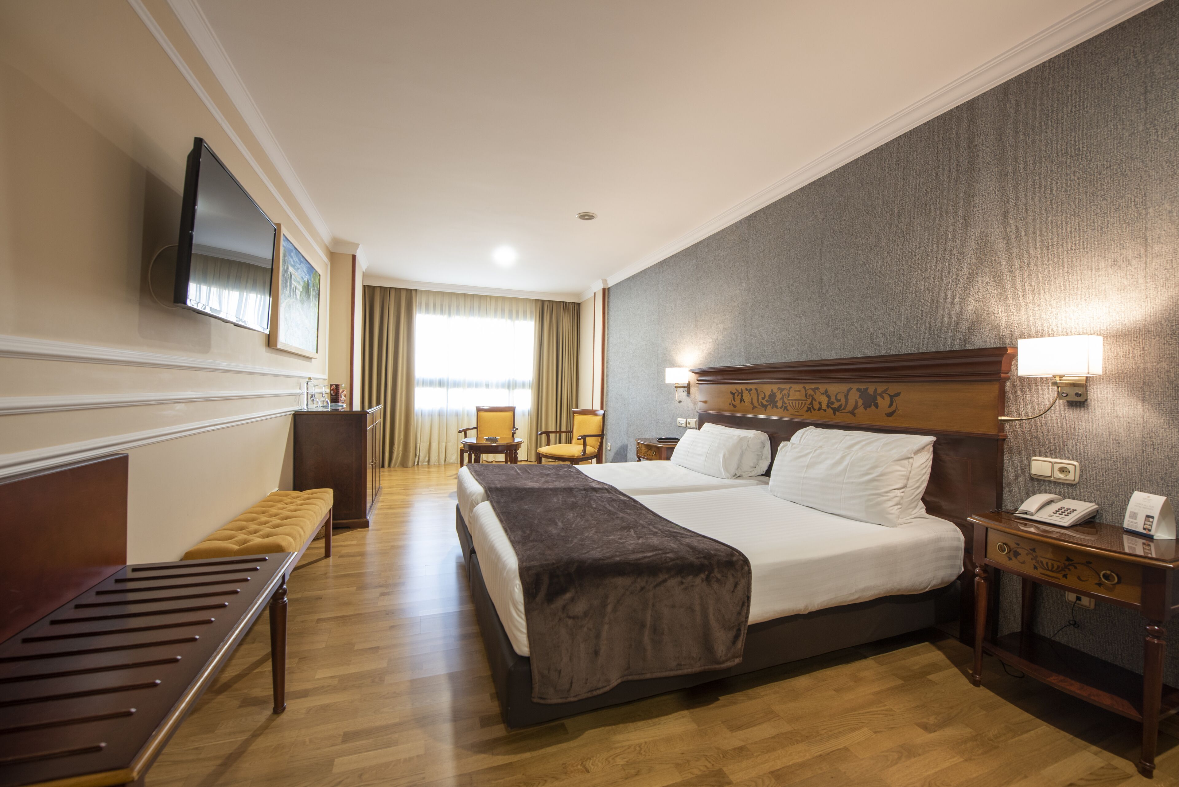 A hotel room with a large bed, a bench, a desk with a phone, and a TV mounted on the wall.