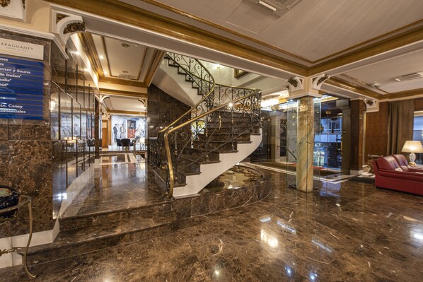 A grand lobby with a marble staircase, a reception desk, and a red leather sofa.