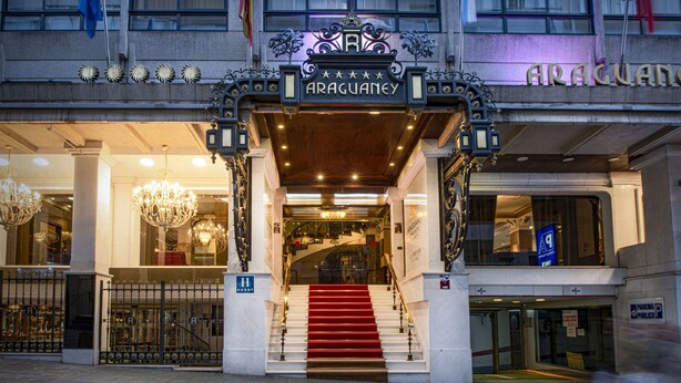 Entrada de un hotel con una escalera monumental, señalización ornamental y un candelabro.