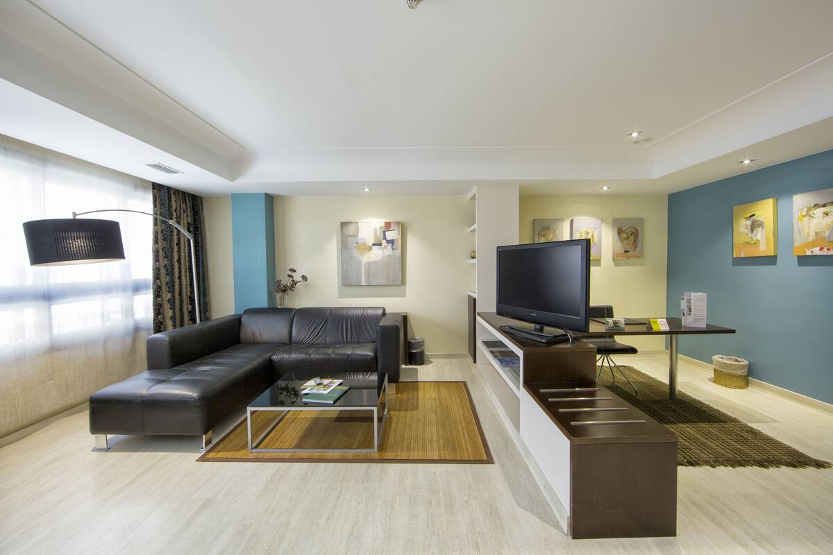 Een moderne woonkamer met een hoekbank, een flatscreen televisie en kunstwerken aan de muur.