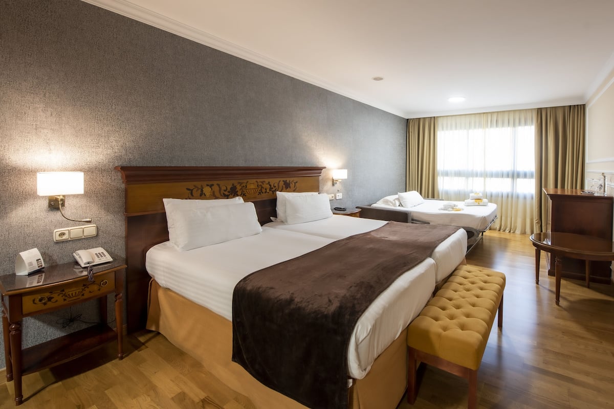 Een hotelkamer met een groot bed, een kleiner bed, een bureau met telefoon en een stoel.