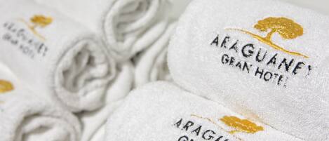 Rolled white towels with embroidered text and a golden tree logo, indicating they are from Araguane Grande Hotel.