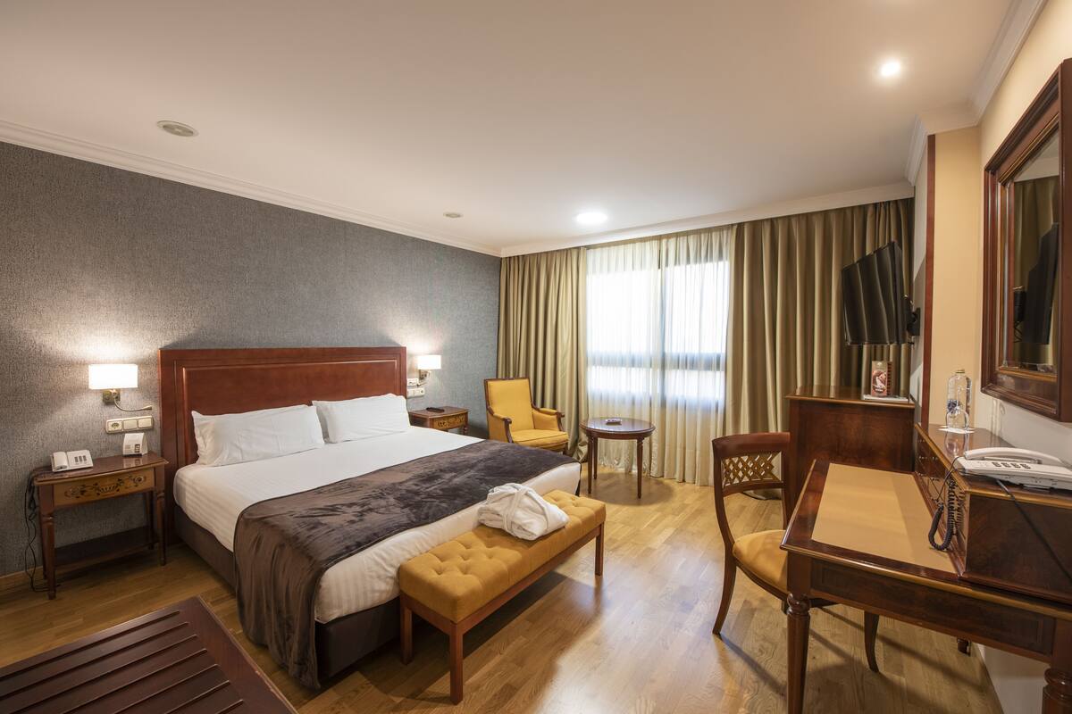 Een hotelkamer met een groot bed, nachtkastjes, een bureau, een stoel, een klein tafeltje en een spiegel.