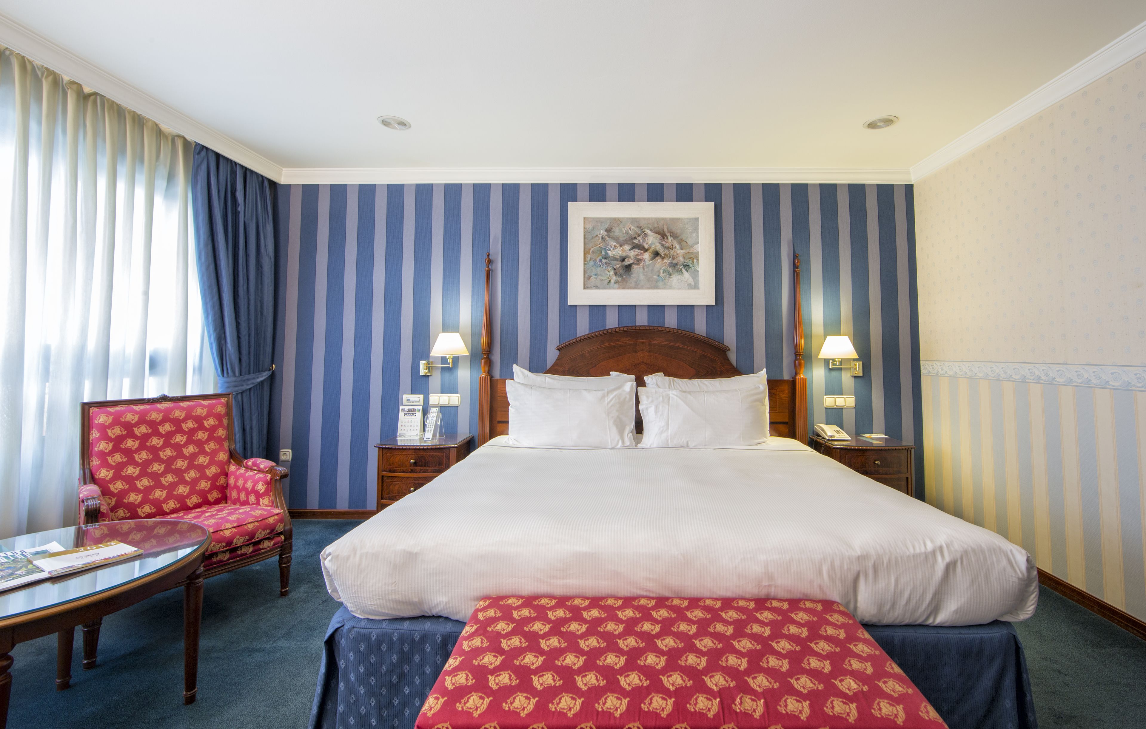 A hotel room with a large bed, a chair, a table, and two bedside lamps.