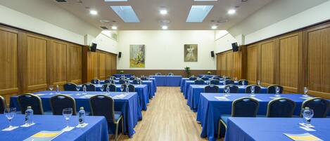 A conference room with multiple tables, each covered with blue tablecloths and equipped with water bottles and glasses.