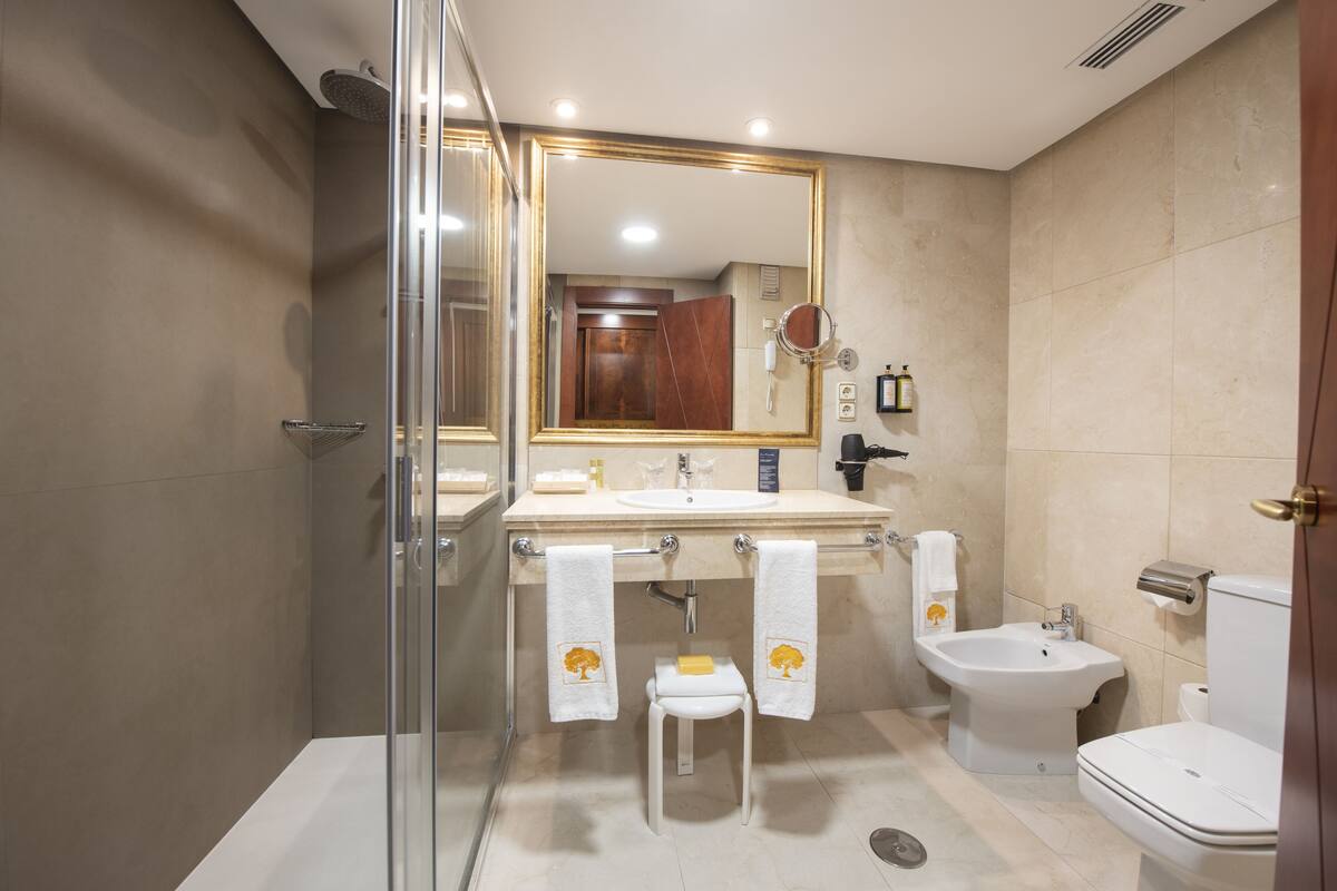 Een moderne badkamer met een douchecabine van glas, een witte wastafel, een toilet en een bidet.