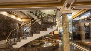 Una imponente escalera de mármol con barandillas metálicas ornamentales, que conduce a un rellano del segundo piso.