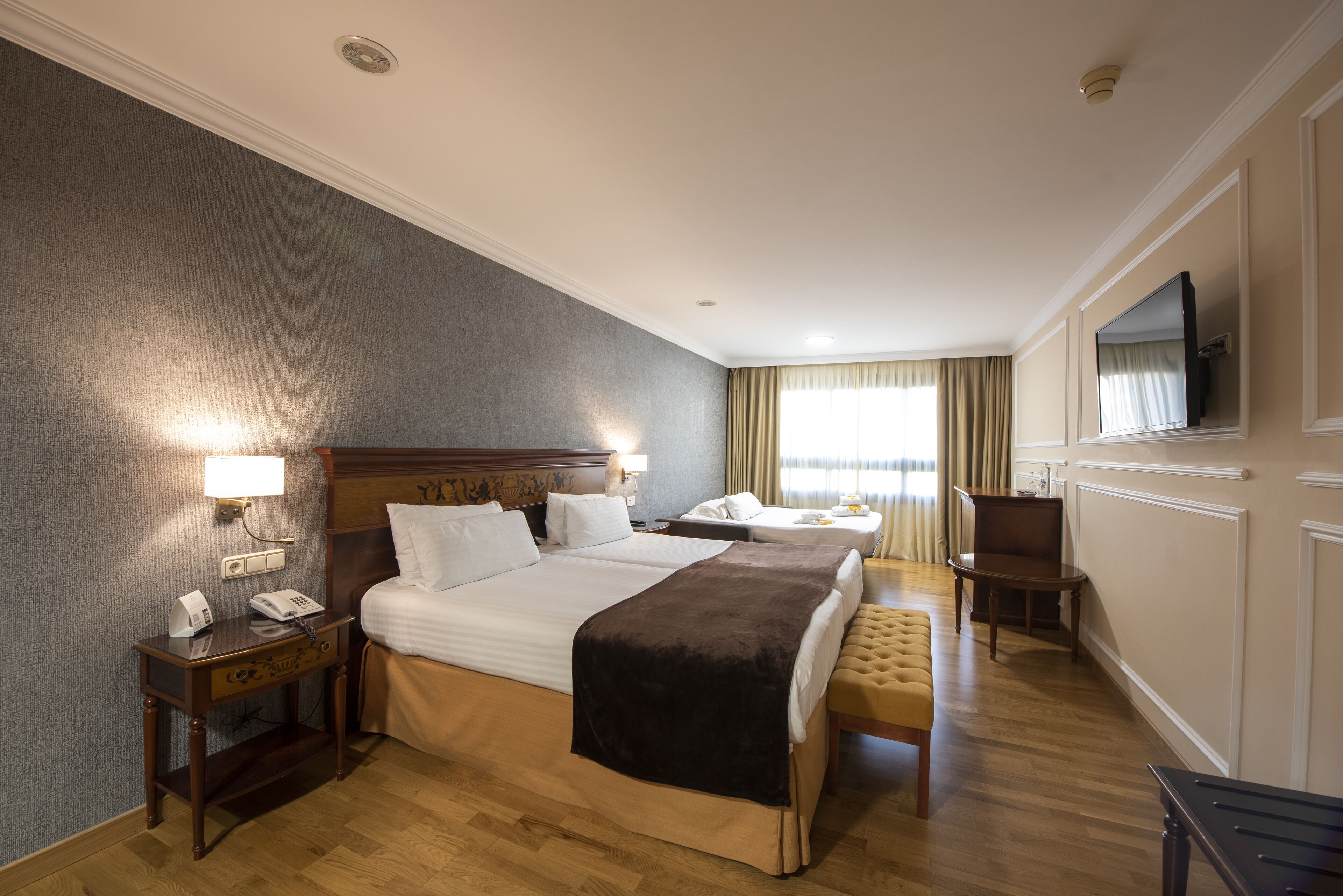 Una habitación de hotel con una cama grande, una mesita de noche con teléfono, una silla, un escritorio y un televisor montado en la pared.
