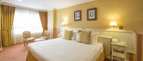 Habitación de hotel con una cama grande, dos mesitas de noche, una silla, un escritorio y un teléfono.