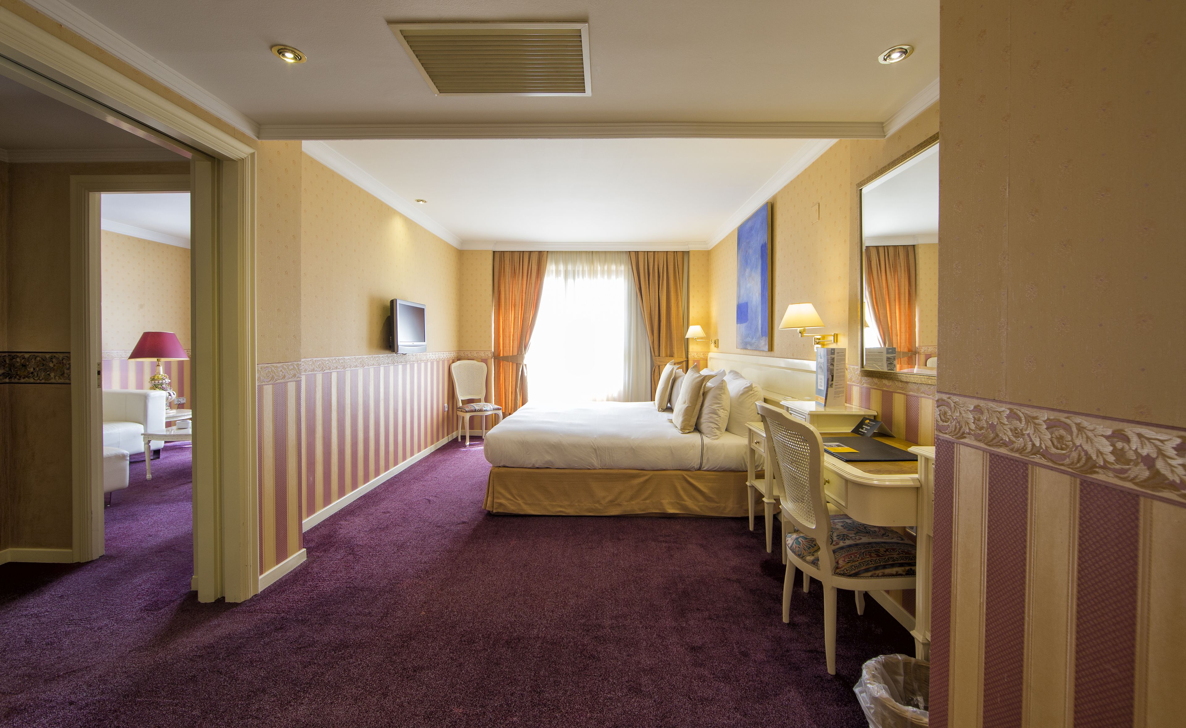 A hotel room with a bed, desk, chair, and a television.