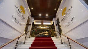Una imponente escalera con alfombra roja que conduce a la entrada de un hotel, flanqueada por paredes blancas y detalles dorados.