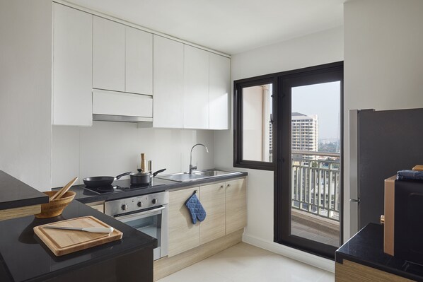 A modern kitchen with white cabinets, a black countertop, a stove, and a window with a city view. - Somerset Park Suanplu Bangkok (Bangkok)