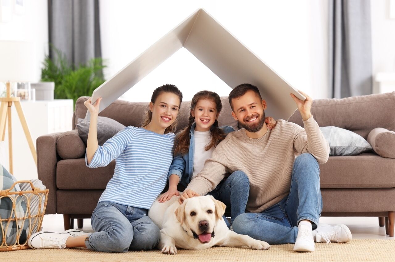 Eine Familie sitzt mit einem Hund auf einem Sofa und hält ein großes, weißes Objekt.