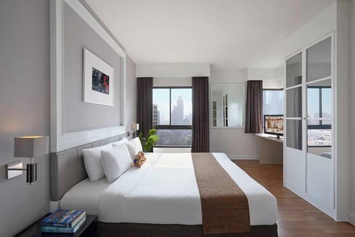 A modern hotel room with a large bed, a city view, a desk, and a window with curtains.