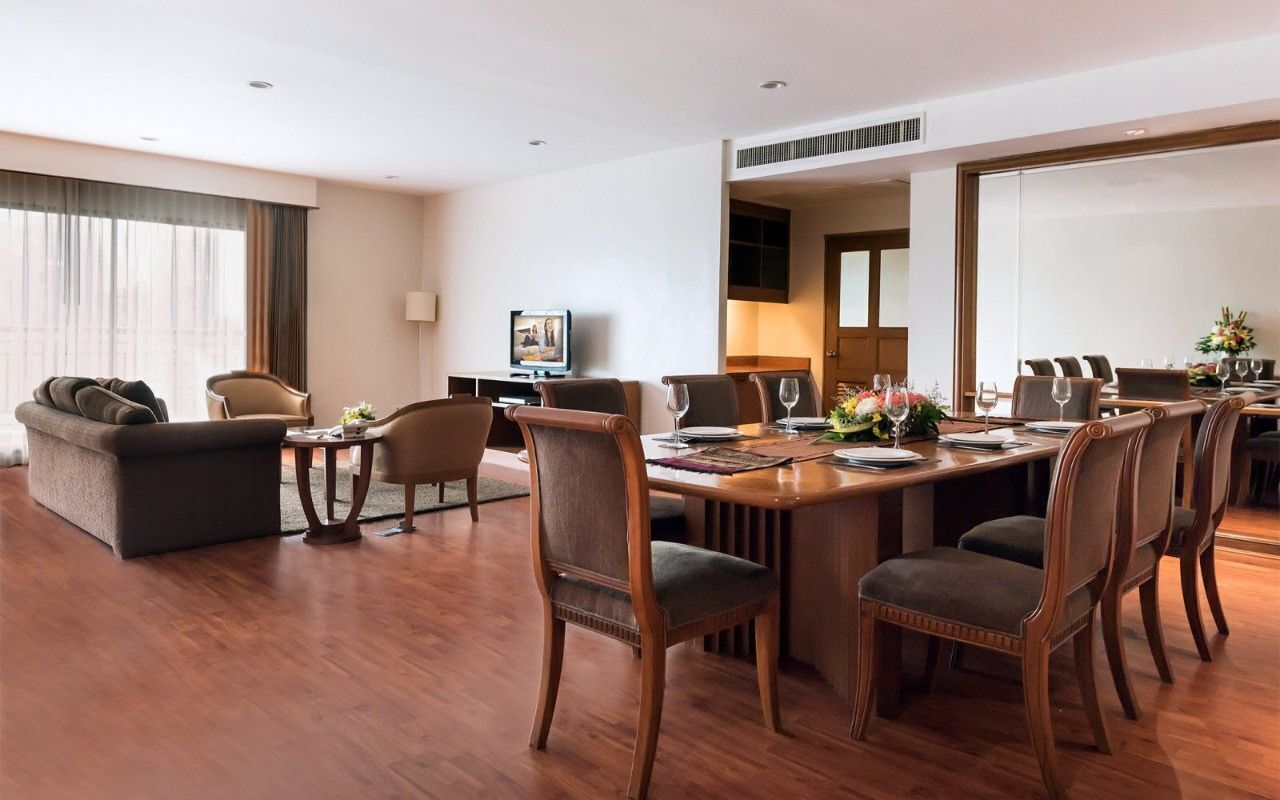 Quarto de hotel com área de refeições, sofá, televisão e uma grande janela.