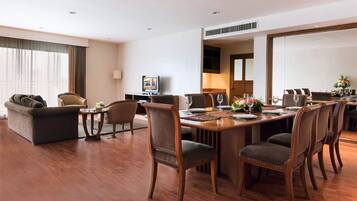 Quarto de hotel com área de refeições, sofá, televisão e uma grande janela.