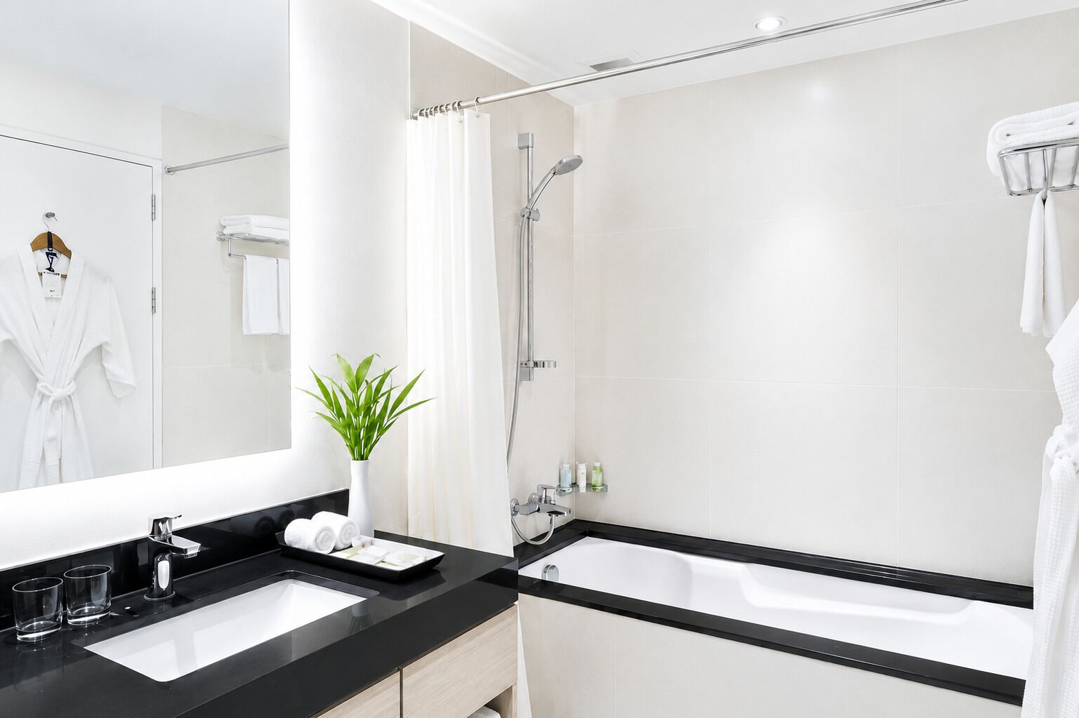 Un bagno moderno con un piano d'appoggio nero, lavandino bianco e una vasca da bagno grande.