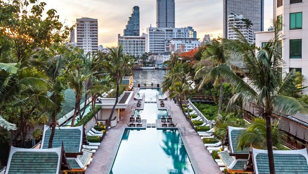 A rooftop pool with lounge chairs and palm trees, surrounded by high-rise buildings.