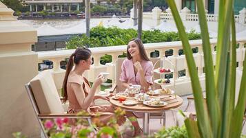 Terraço com mesa posta para dois, com vista para um corpo de água e edifícios ao fundo.