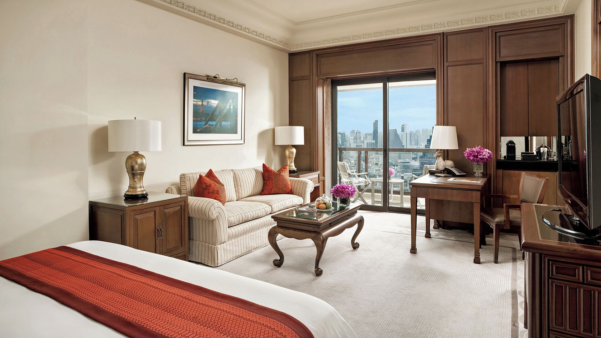 A hotel room with a bed, a sofa, a desk, a chair, a coffee table, and a television.