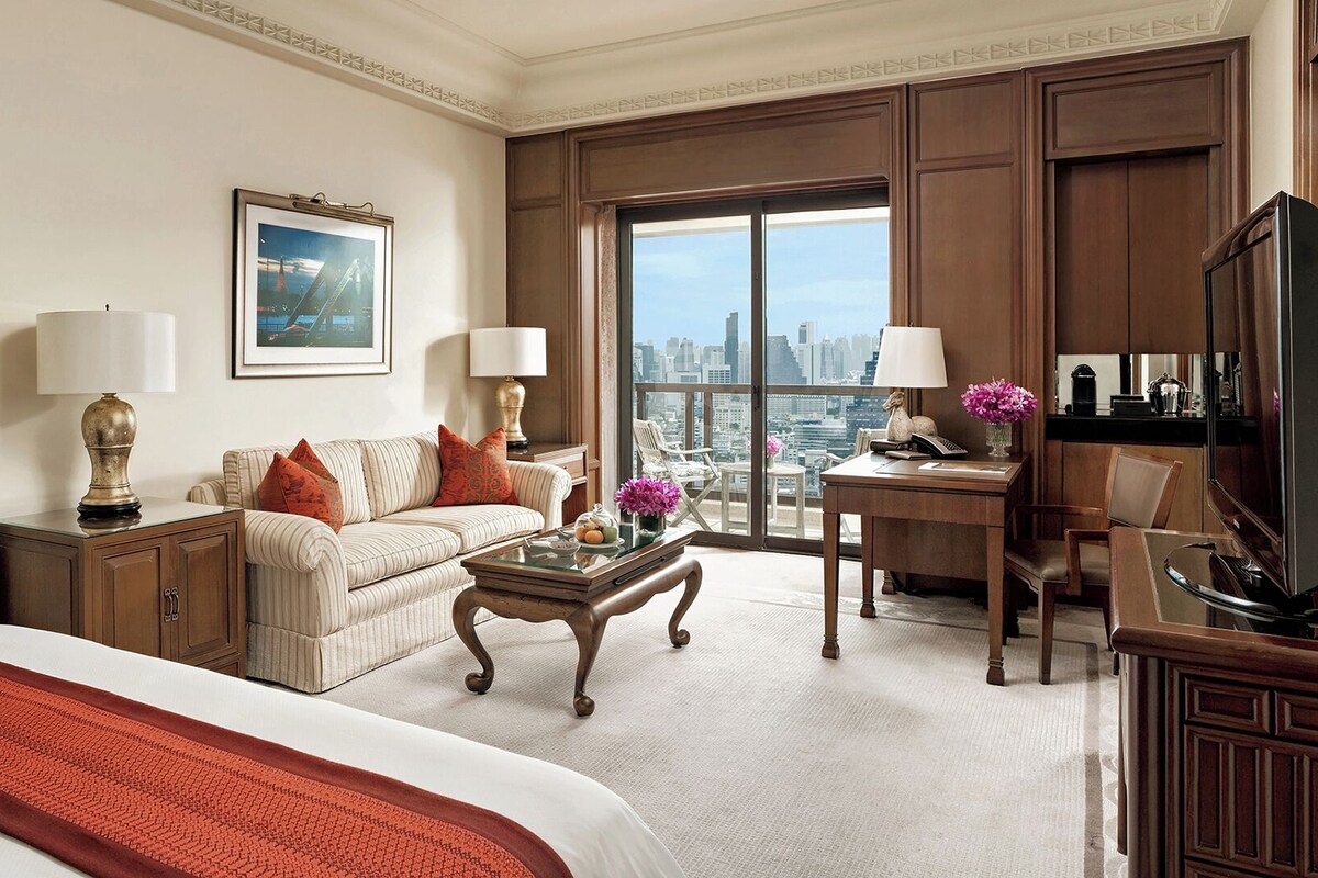 A hotel room with a bed, a sofa, a desk, a chair, a coffee table, and a television.