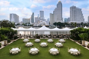 A rooftop dining area with round tables and chairs, overlooking a city skyline and a body of water.