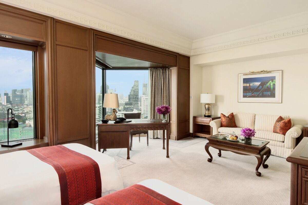 A hotel room with a large bed, a desk, a coffee table, a sofa, and a city view.