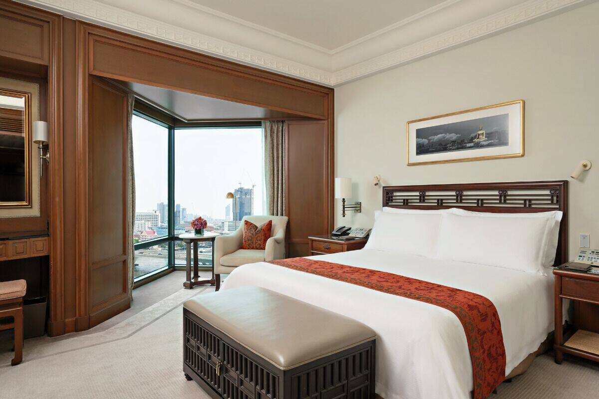Ein Hotelzimmer mit einem großen Bett, einem Sessel, einem Schreibtisch und Blick auf die Stadt.