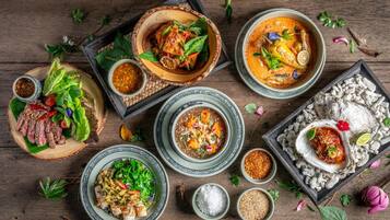 A variety of dishes including seafood, salads, and bowls of soup, arranged on a wooden table with various condiments and herbs.
