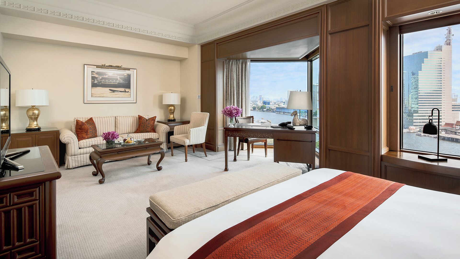 A hotel room with a bed, a desk, a chair, a sofa, and a view of the city.