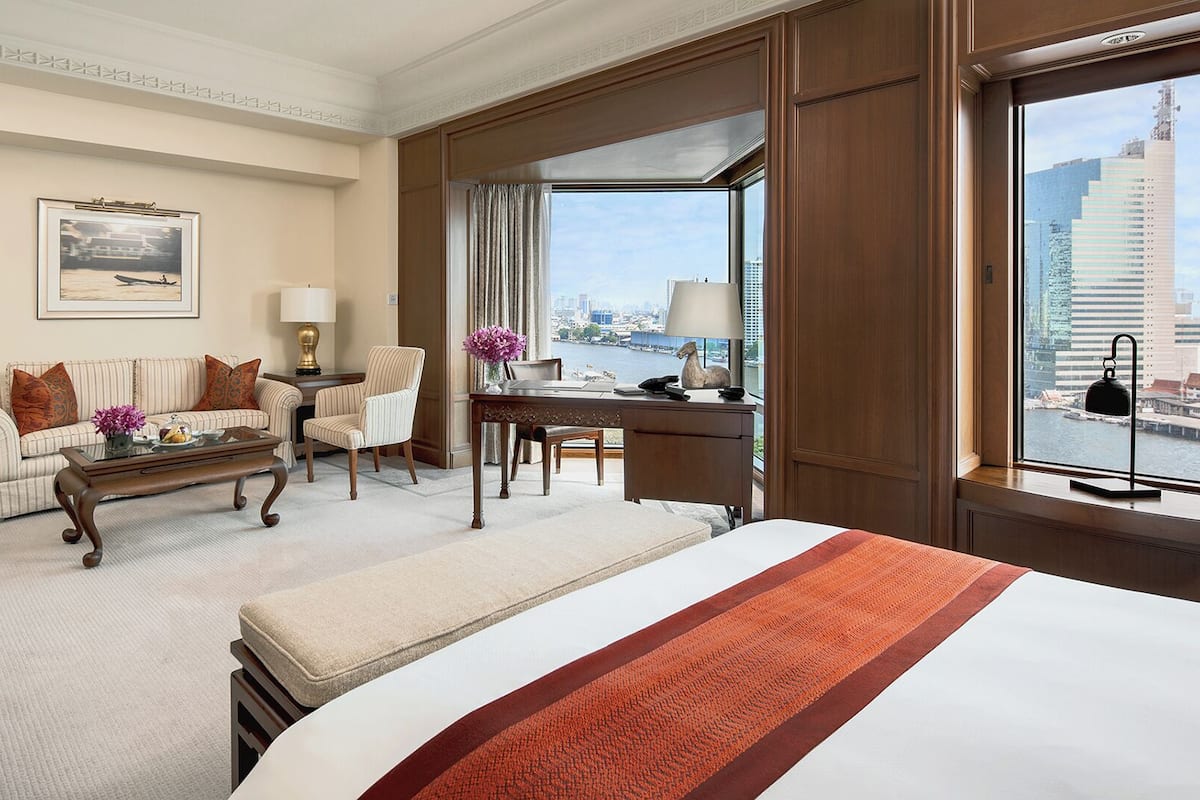 A hotel room with a bed, a desk, a chair, a sofa, and a view of the city.