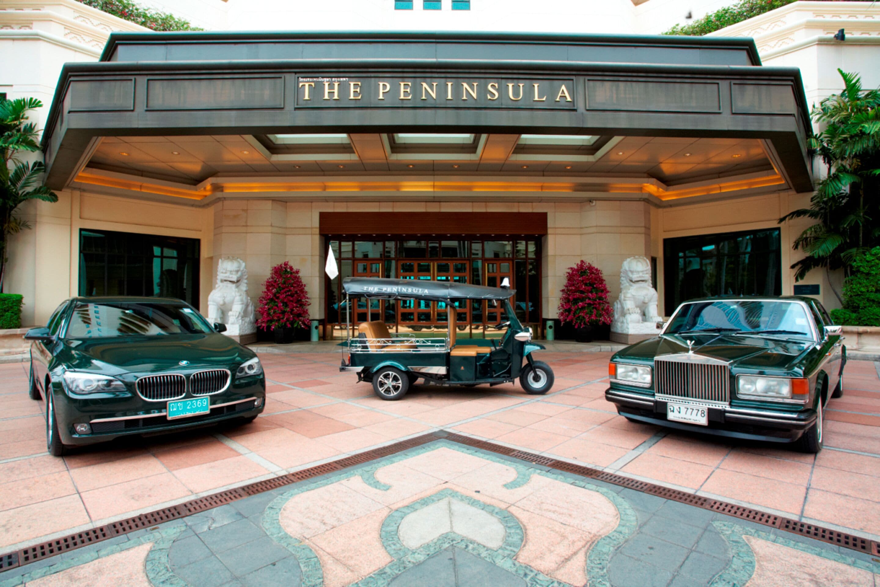 A grand entrance with a classic car and a vintage vehicle parked in front of a building labeled "The Peninsula."