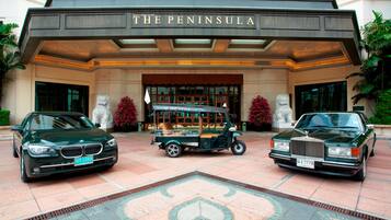 A grand entrance with a classic car and a vintage vehicle parked in front of a building labeled "The Peninsula."