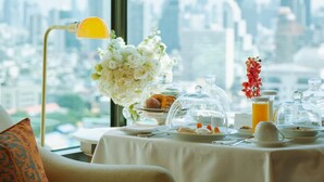 A breakfast setting with a city view, including a table with breakfast items, a vase of flowers, and a lamp.