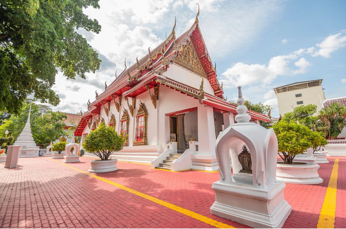 Un temple thaïlandais traditionnel, avec une façade rouge et blanche, des colonnes blanches et un escalier central menant à l’entrée.