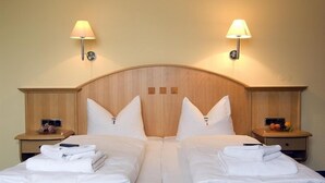 Una cama doble con ropa de cama blanca, dos mesitas de noche con lámparas y un cabecero de madera.