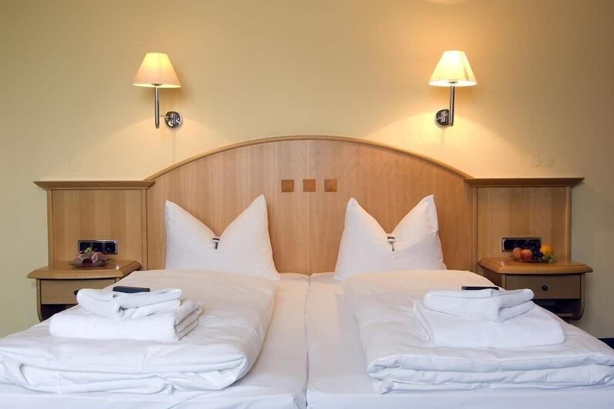 A double bed with white linens, two bedside tables with lamps, and a wooden headboard.