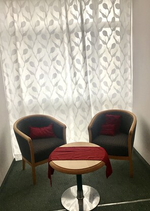 Una habitación con dos sillones, una mesita y una cortina estampada, con piso verde.