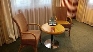 Una habitación de hotel con dos sillones de mimbre, una mesita redonda con una bandeja de botellas y vasos, y una lámpara.