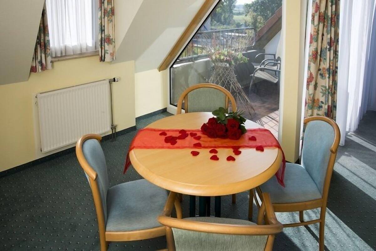 A dining area with a round table, four chairs, and a view of the outside through a large window.