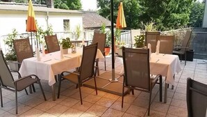 Un patio al aire libre con mesas y sillas, rodeado de plantas en macetas y sombrillas.