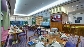 A modern restaurant with multiple dining tables, chairs, and a bar area.