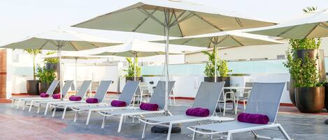 A rooftop lounge area with sunbeds and umbrellas.