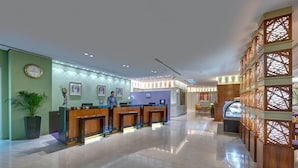 Een moderne hotellobby met een receptiebalie, ingelijste foto’s aan de muur en een decoratieve houten scheidingswand.